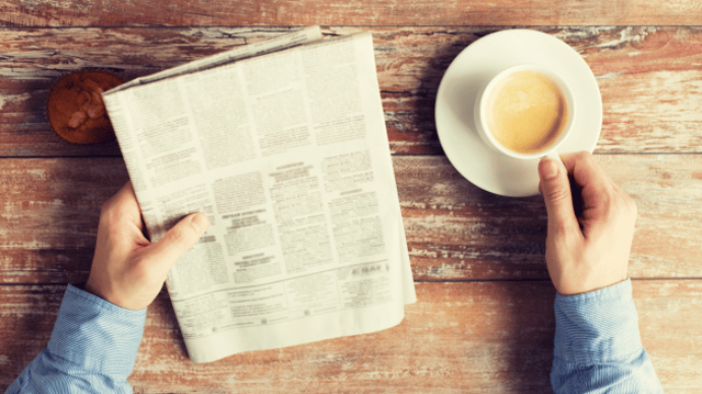 Pessoa lê jornal e toma café