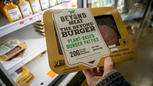 pessoa segura hambúrguer vegano da Beyond Meat no mercado em frente à geladeira.