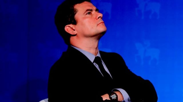 Sérgio Moro de braços cruzados em frente à um fundo azul