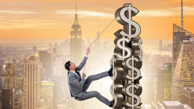 Homem escala torre feita de cifras de dinheiro