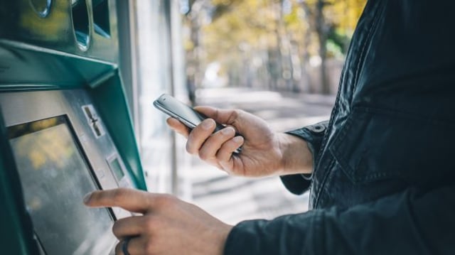 mãos masculinas usando telefone inteligente enquanto digita em ATM, caixa eletrônico de banco | Banco Central Bancos Digitais