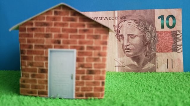 Imagem conceitual mostra nota de dez reais e uma casa