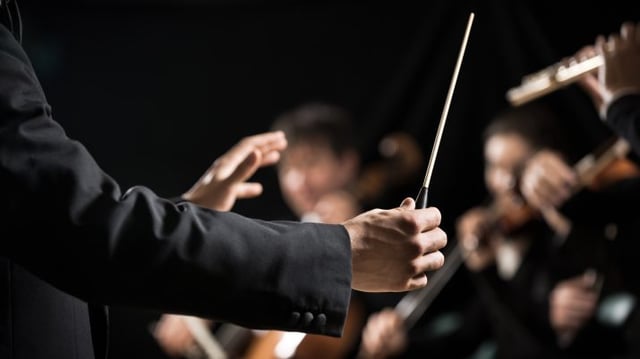 Conductor,Directing,Symphony,Orchestra,With,Performers,On,Background,,Hands,Close-up.