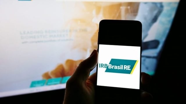 Imagem de um celular com o logo do IRB (IRBR3) sendo exibido na tela | Ibovespa