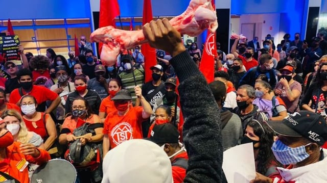 Integrante do MTST segurando um osso bovino em primeiro plano, com outros manifestantes vestidos de vermelho ocupando a sede da B3