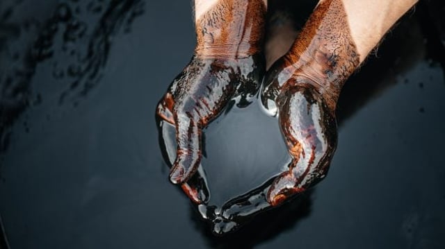 Mãos em concha segurando um líquido escuro, parecido com petróleo