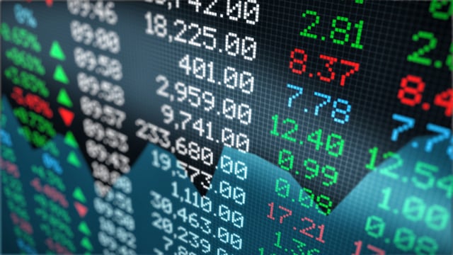 O preço de ações é exibido em uma tela, com diversos valores em verde e vermelho