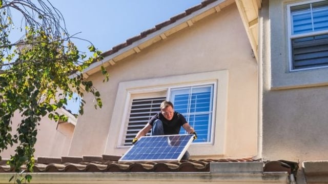 Homem instala painel solar em telhado de casa