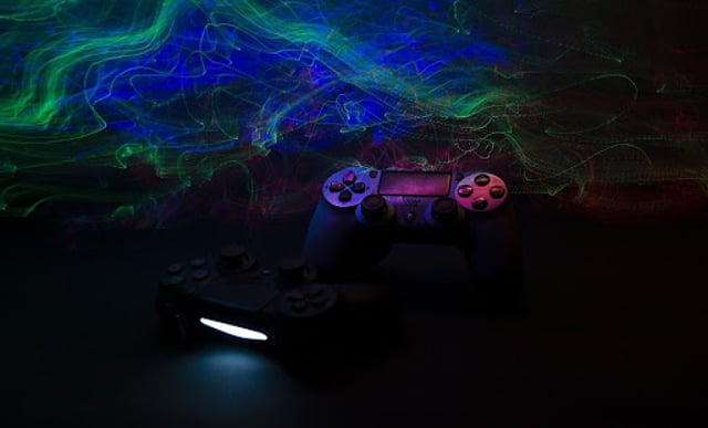 O fundo é verde e azul, com um controle preto de Playstation na frente.