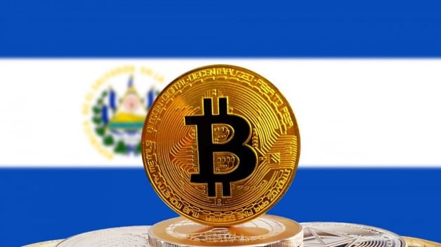 Montagem com um Bitcoin (BTC) no primeiro plano e, ao fundo, uma bandeira de El Salvador aparece desfocada