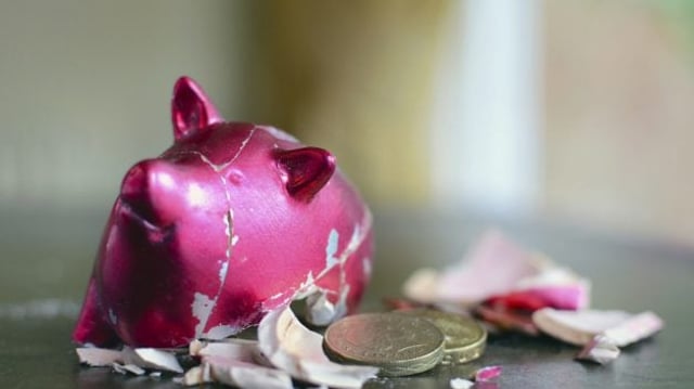Cofrinho cor de rosa em formato de porco esmagado e com moedas caídas para fora | Poupança