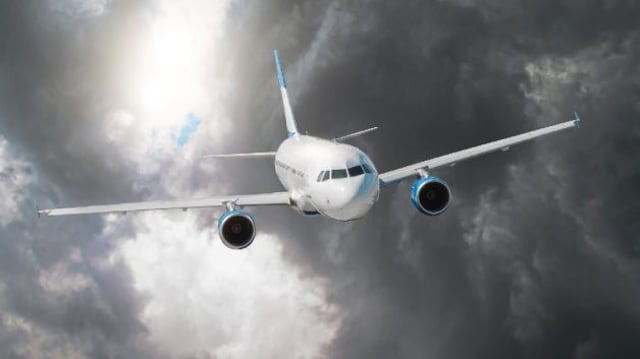 Avião sobrevoando um céu cinzento e carregado, simbolizando problemas no setor aéreo