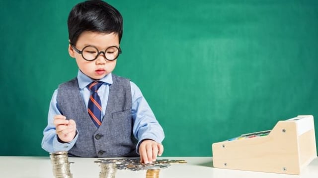 Criança com óculos e roupa social empilhando moedas em cima da mesa