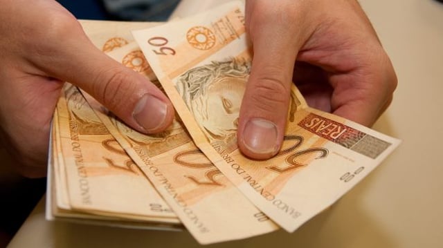 Mão segurando notas de dinheiro (real), cada nota de cinquenta reais