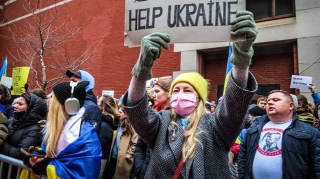 Mulher segura um cartaz escrito em inglês Stop War em meio a manifestantes com bandeira da Ucrânia | Rússia