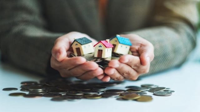homem segura miniatura de casas e moedas | Casa Verde e Amarela, ações, incorporadoras