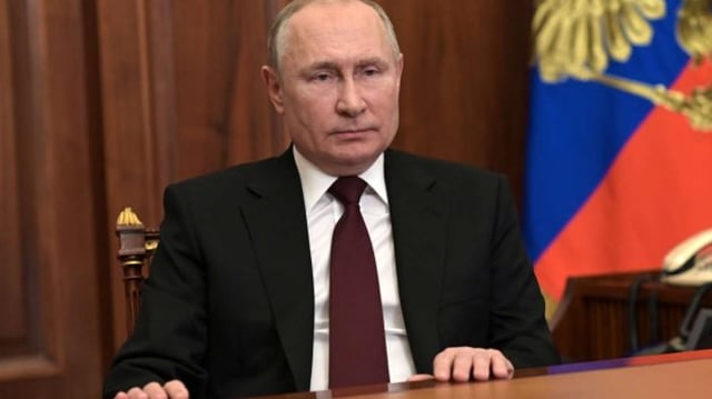 Presidente russo, Vladimir Putin, sentado com as mãos sobre uma mesa e com a bandeira da Rússia atrás