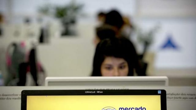 vagas; mulher mexendo no computador ao fundo; no primeiro plano, imagem do logo do Mercado Livre em tela de computador
