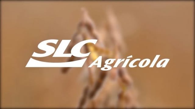 Logo da SLC Agrícola (SLCE3) em branco, no primeiro plano. Ao fundo, desfocado, aparece um broto de soja