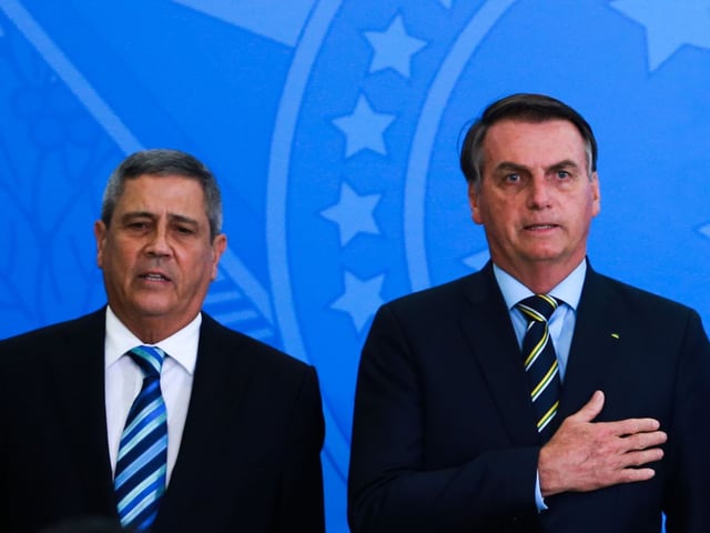 Braga Netto ao lado do presidente Jair Bolsonato, que leva a mão ao peito