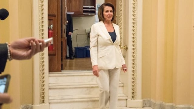 Nancy Pelosi, a presidente da Câmara dos EUA, desce escadas com um terno branco e blusa azul