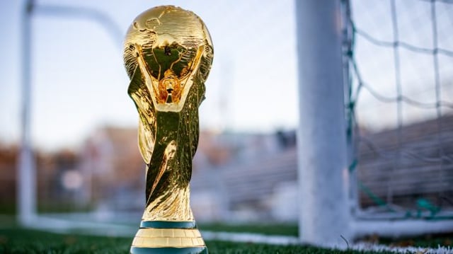 Troféu dourado da Copa do Mundo atrás do gol e sob gramado verde