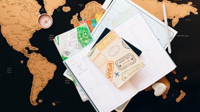 Mapa Mundi em preto e bege ao fundo com outros mapas em papel sobrepostos e passaporte