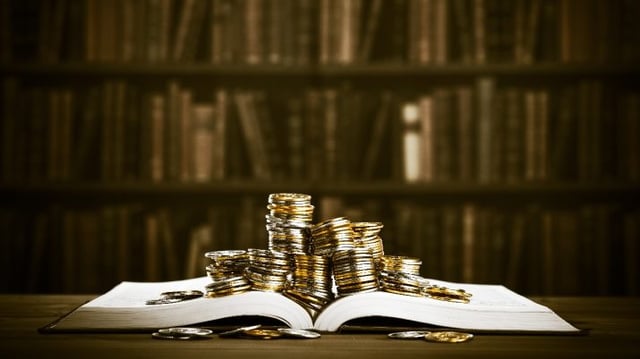 Um livro aberto com moedas no topo, simbolizando o aprendizado sobre investimentos; há mais livros ao fundo