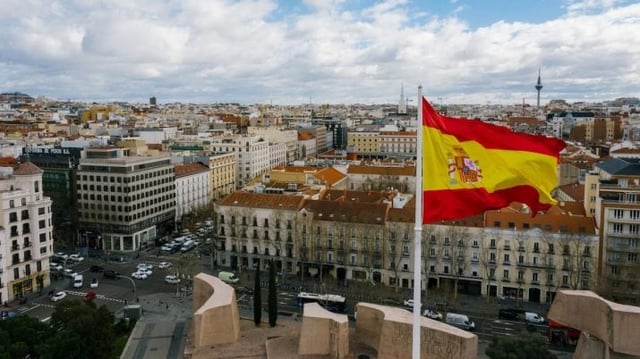 Bandeira da Espanha, em primeiro plano, com um ambiente urbano ao fundo