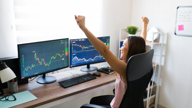 Investidora mulher comemorando enquanto olha para tela de computador com gráficos