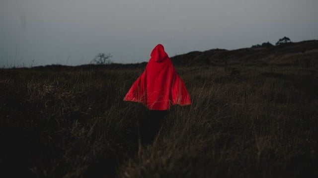 Mulher de capuz vermelho andando em descampado