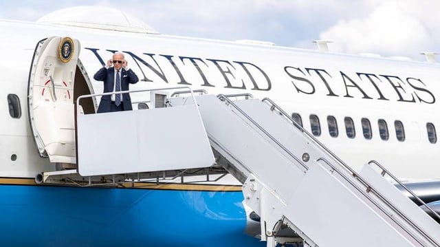 O presidente dos EUA, Joe Biden, aparece de pé, na porta do avião Air Force 1, colando óculos escuros