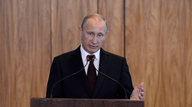 O presidente da Rússia, Vladimir Putin, de terno preto, em pé, na frente de um púlpito