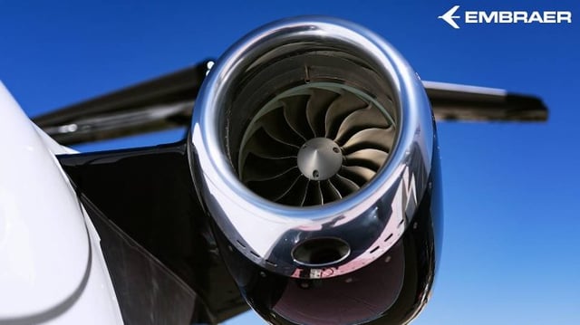 Foto de um céu azul, com a turbina de uma das asas de um avião da Embraer em destaque