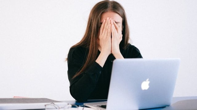 Mulher com o rosto entre as mãos, em frente ao computador, após demissão