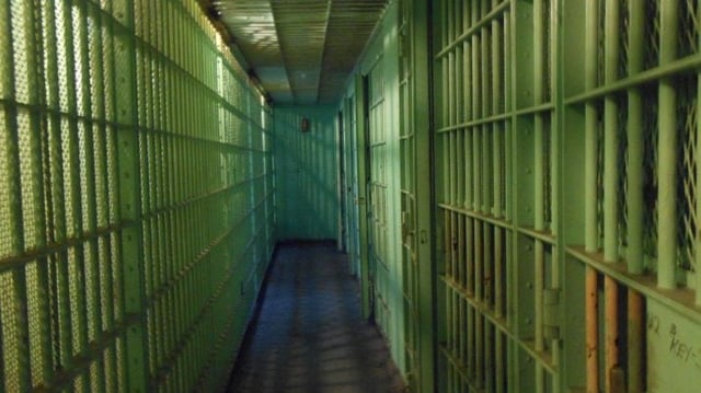 Imagem de um corredor escuro de uma cadeia, com celas pintadas de verde claro
