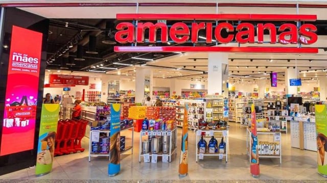 Fachada de uma loja Americanas. É possível ver produtos da loja e um painel na lateral esquerda de dia das mães