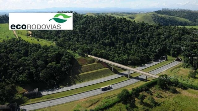 Duas estradas cortadas por uma ponte. Há um caminhão em uma das pontes. Ao redor, montanhas e vegetação. No final das pistas, há dois túneis. Imagem do logo da EcoRodovias com fundo branco, na lateral superior esquerda