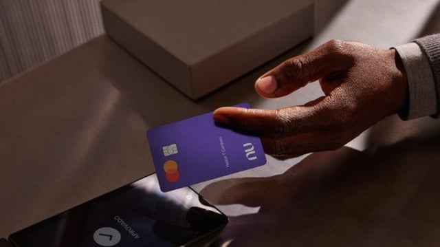 Homem aproxima cartão roxo do Nubank a uum celular