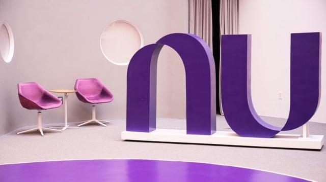 Ambiente com duas cadeiras roxas na lateral e símbolo do Nubank no centro