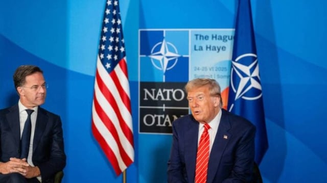 Imagem mostra Donald Trump vestindo terno azul e gravata vermelha. Ele está sentando em uma cadeira ao lado do presidente da Otan, Mark Rutte, que também usa terno escuro e camisa branca. De fundo, a bandeira dos EUA e o símbolo da Otan.
