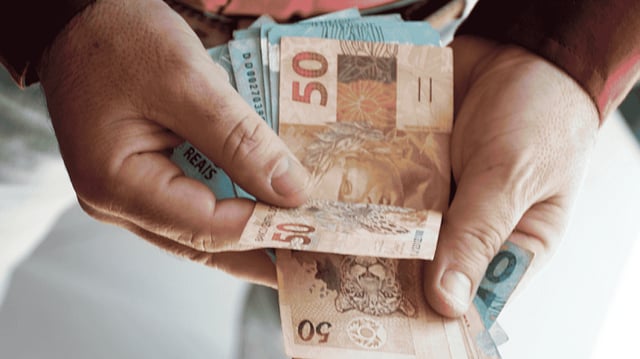 Mãos segurando diversas notas de cinquenta reais.