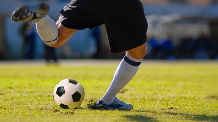 Um jogador de futebol chuta uma bola de futebol em um campo