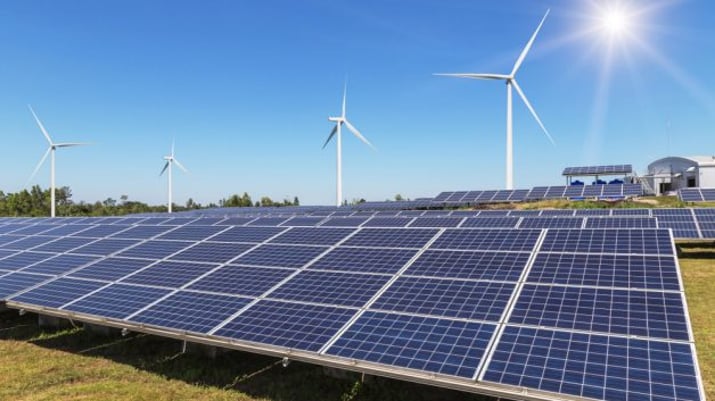 Imagem mostra painéis de energia solar com pás eólicas ao fundo