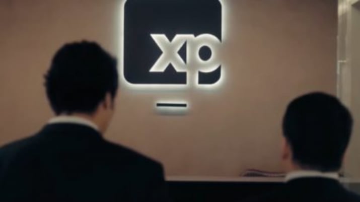 Foto mostrando dois homens olhando para o logo da XP (XPBR31) numa parede