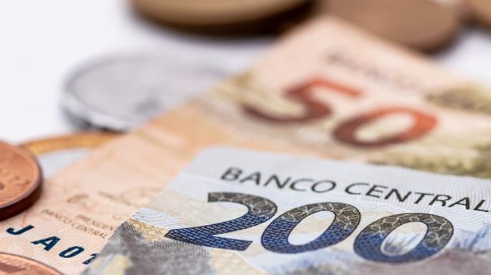 Notas de 50 e 200 reais + moedas expostas em uma mesa