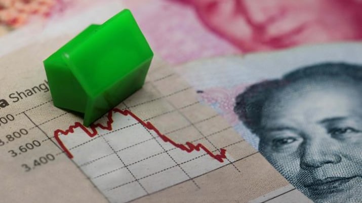 Miniatura verde em formato de casa caída sobre uma gráfico ilustrando a situação do setor imobiliário da China