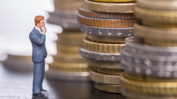 Miniatura de um homem encarando pilhas de moedas | bolsa dividendos