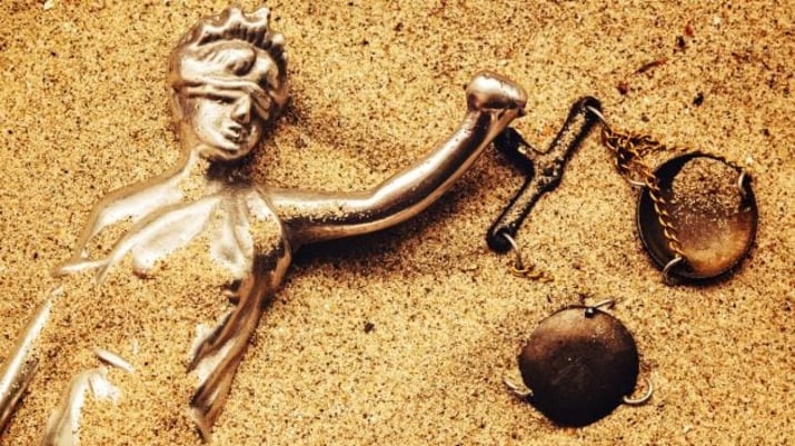 Estátua da senhora Justiça com escala enterrada em areia | Precatórios