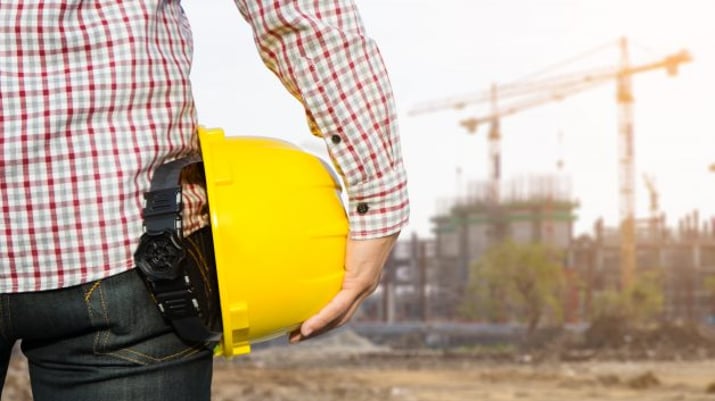 Engenheiro parado em frente a um canteiro de obras segura um capacete de segurança amarelo | Incorporadoras, ações